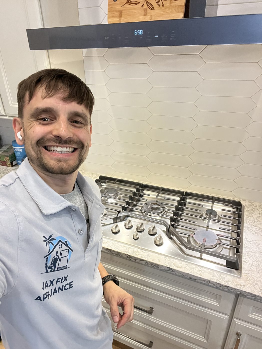 Konstantin in a branded Jax Fix Appliance polo next to a stainless gas cooktop