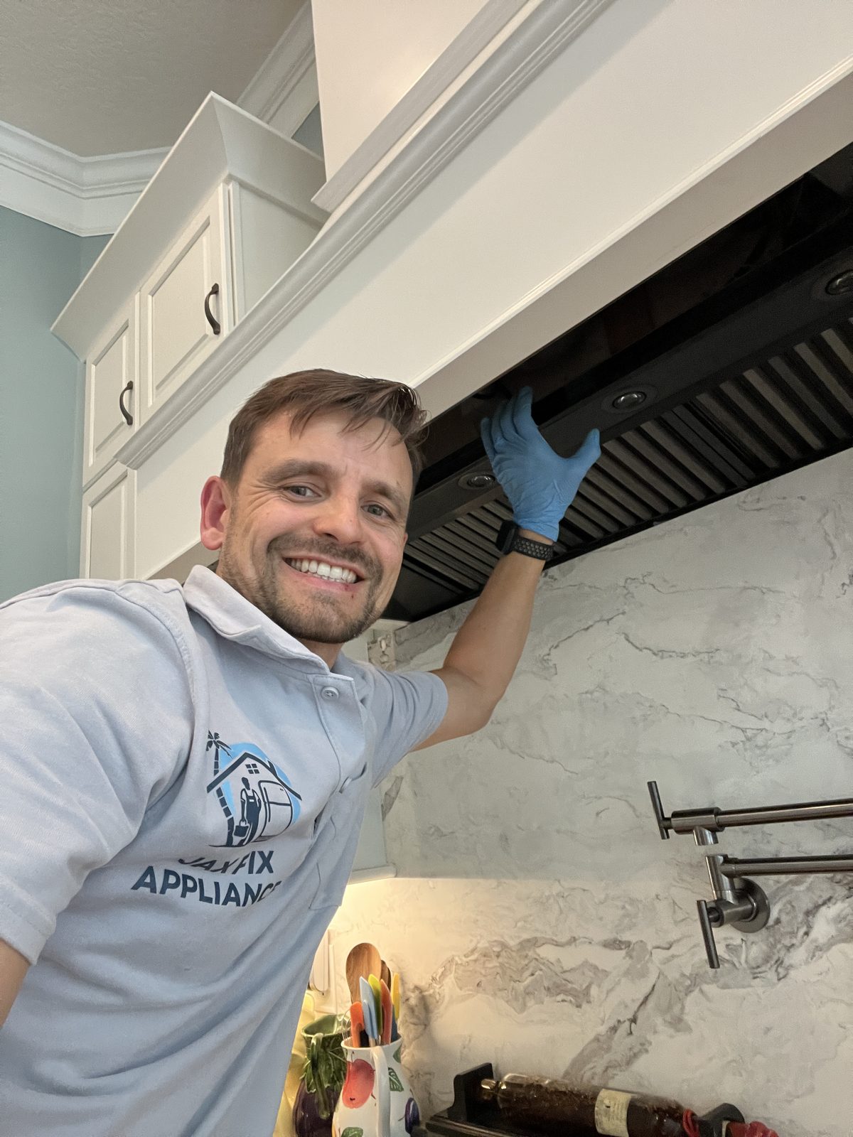 Konstantin servicing a range hood over a marble backsplash kitchen