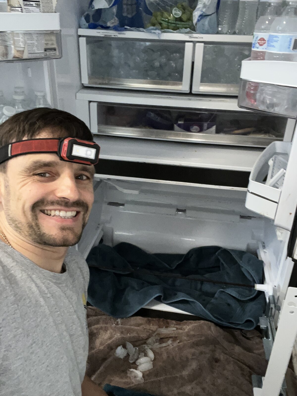 Konstantin servicing a side-by-side refrigerator interior with headlamp