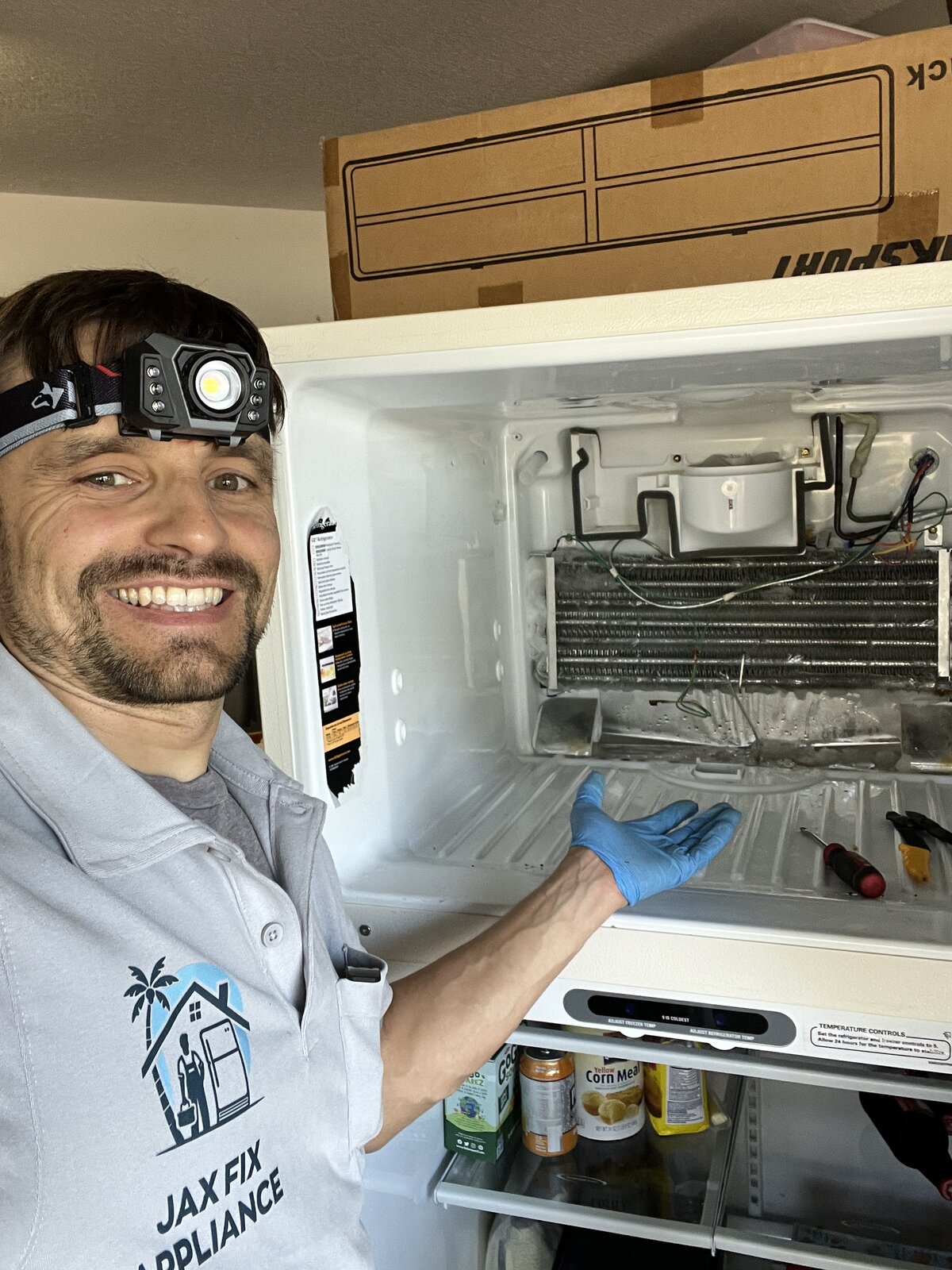 Konstantin in branded Jax Fix Appliance polo at a refrigerator with exposed evaporator coils