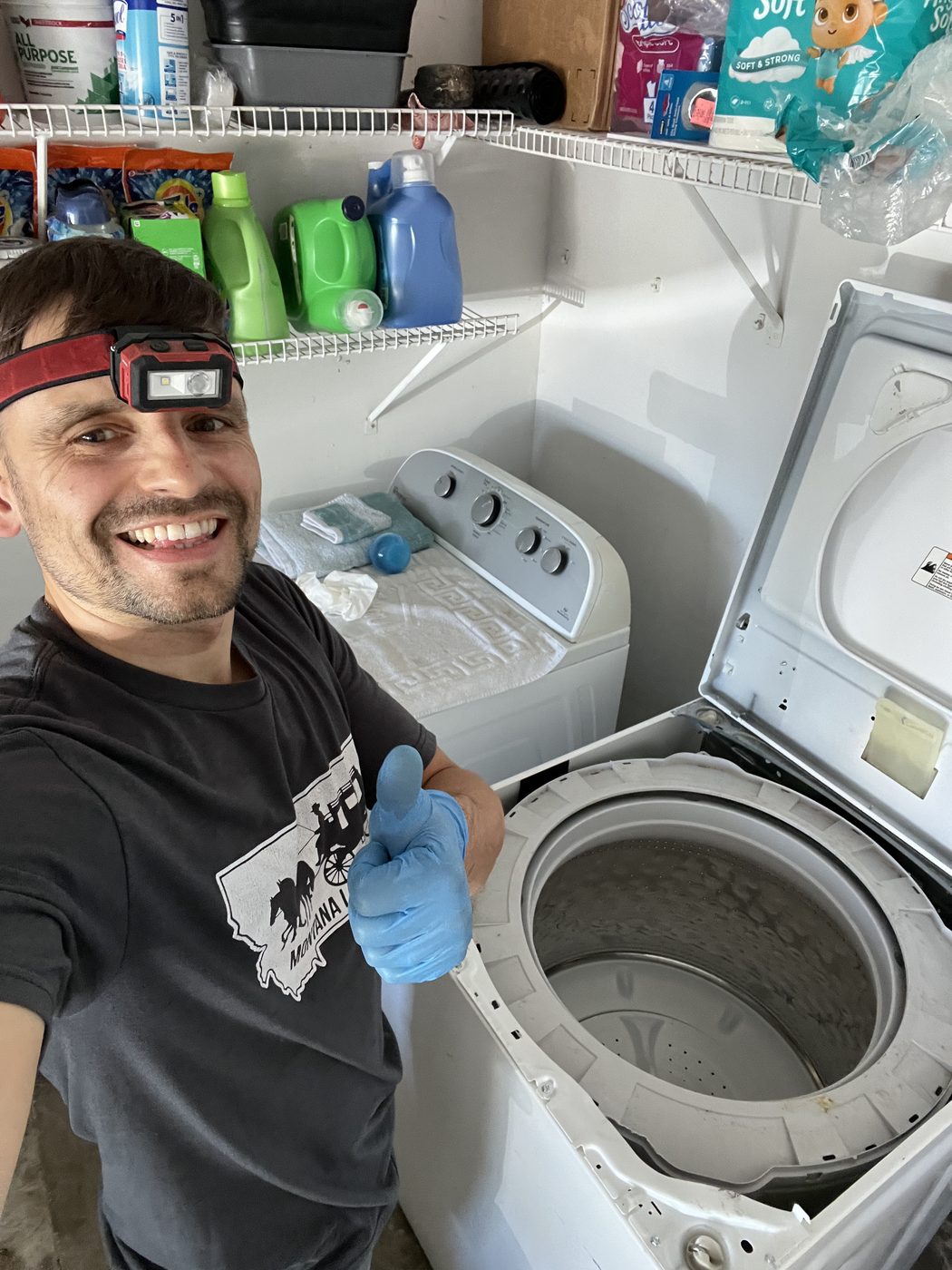 Konstantin next to an open top-load washer drum mid-repair